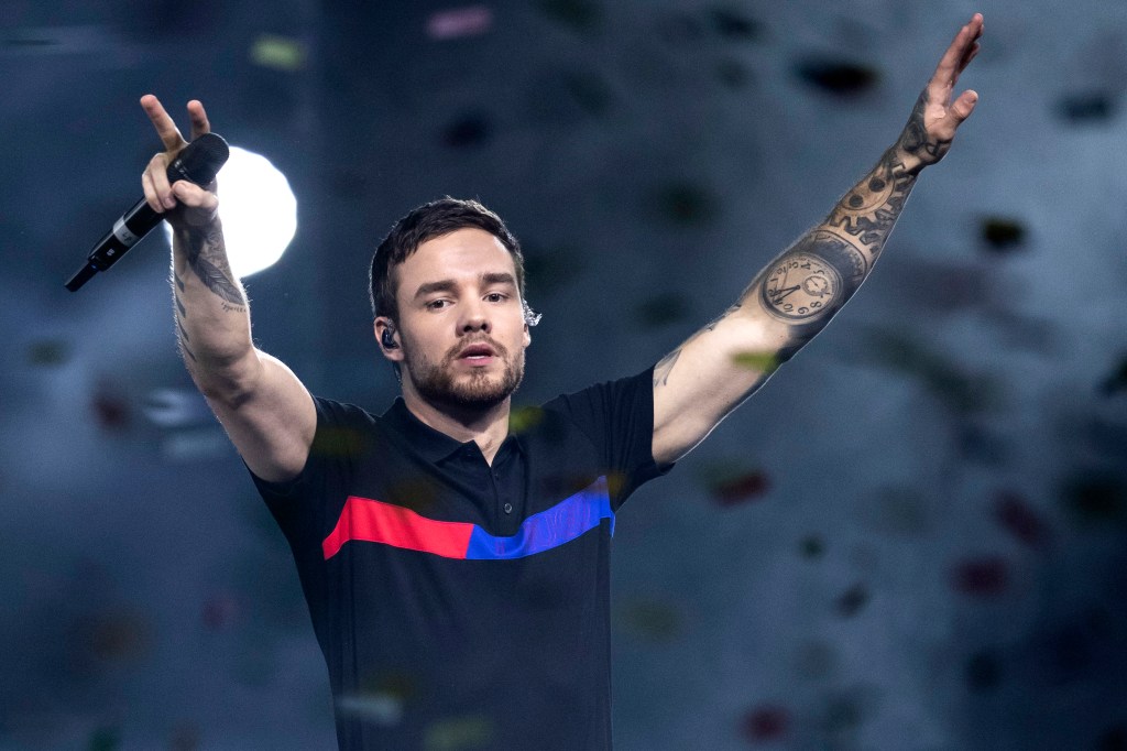 Liam Payne performing on stage, raising his arms in the air and holding a microphone