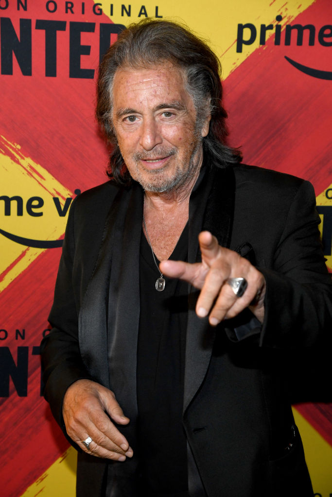 Al Pacino posing at a red carpet event wearing a black t-shirt and a black suit jacket