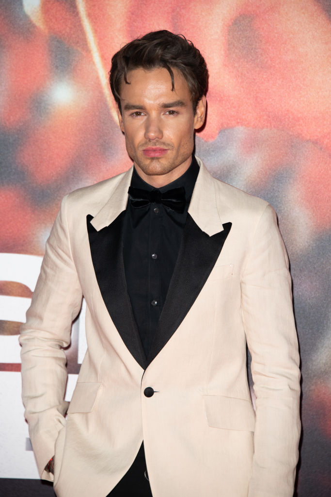 Liam Payne posing at a red carpet event wearing a black shirt and a pink suit jacket