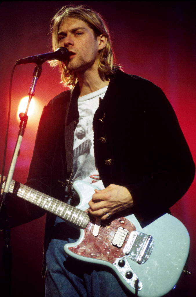 Kurt Cobain singing into a microphone while playing guitar onstage