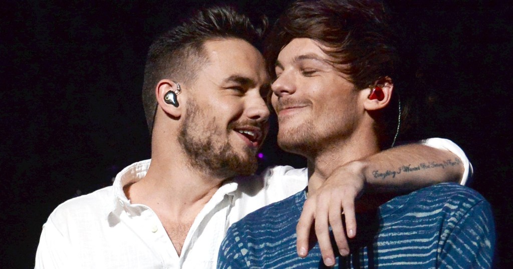 Liam Payne smiles on stage looking at Louis Tomlinson