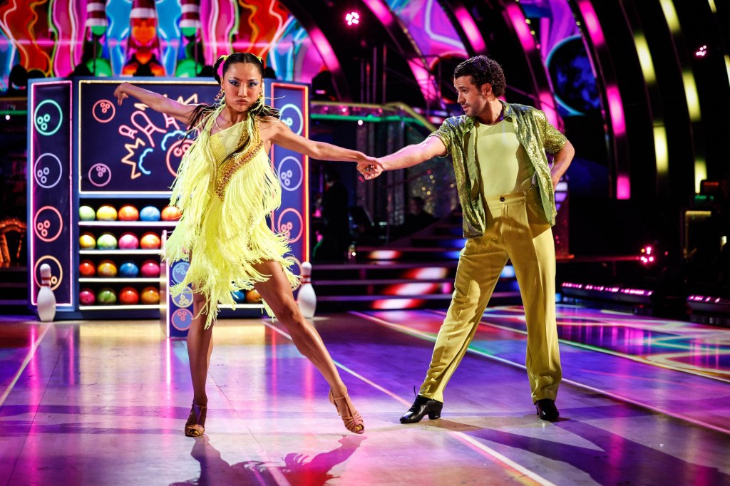 Shayne Ward and Nancy Xu holding hands and dancing with their feet wide apart on Strictly Come Dancing. They are in lime green outfits.