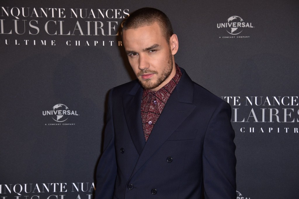 Liam Payne looks into the camera as he poses in a dark jacket and red shirt at an event