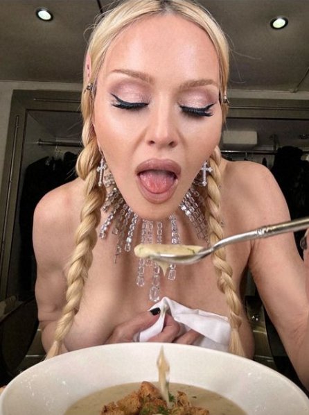 Madonna opens her mouth to eat soup, while topless and wearing a large crystal necklace