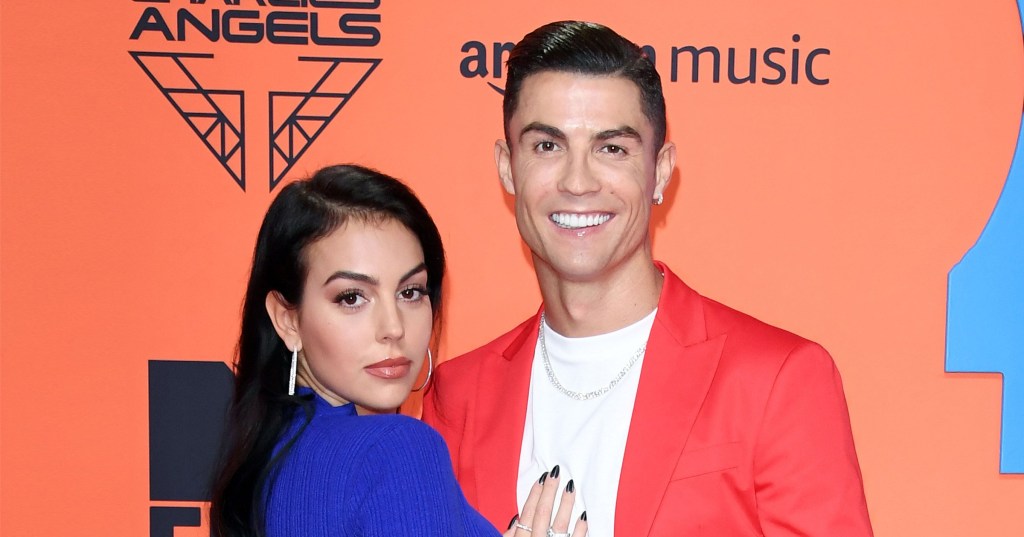 Georgina Rodriguez and Christiano Ronaldo attending an event. Georgina is wearing a blue dress while Christiano wears a white t-shirt and a red blazer