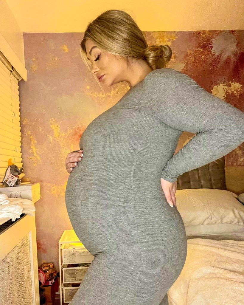 Shaughna Phillips poses on side and shows off pregnant belly in a long-sleeved grey dress